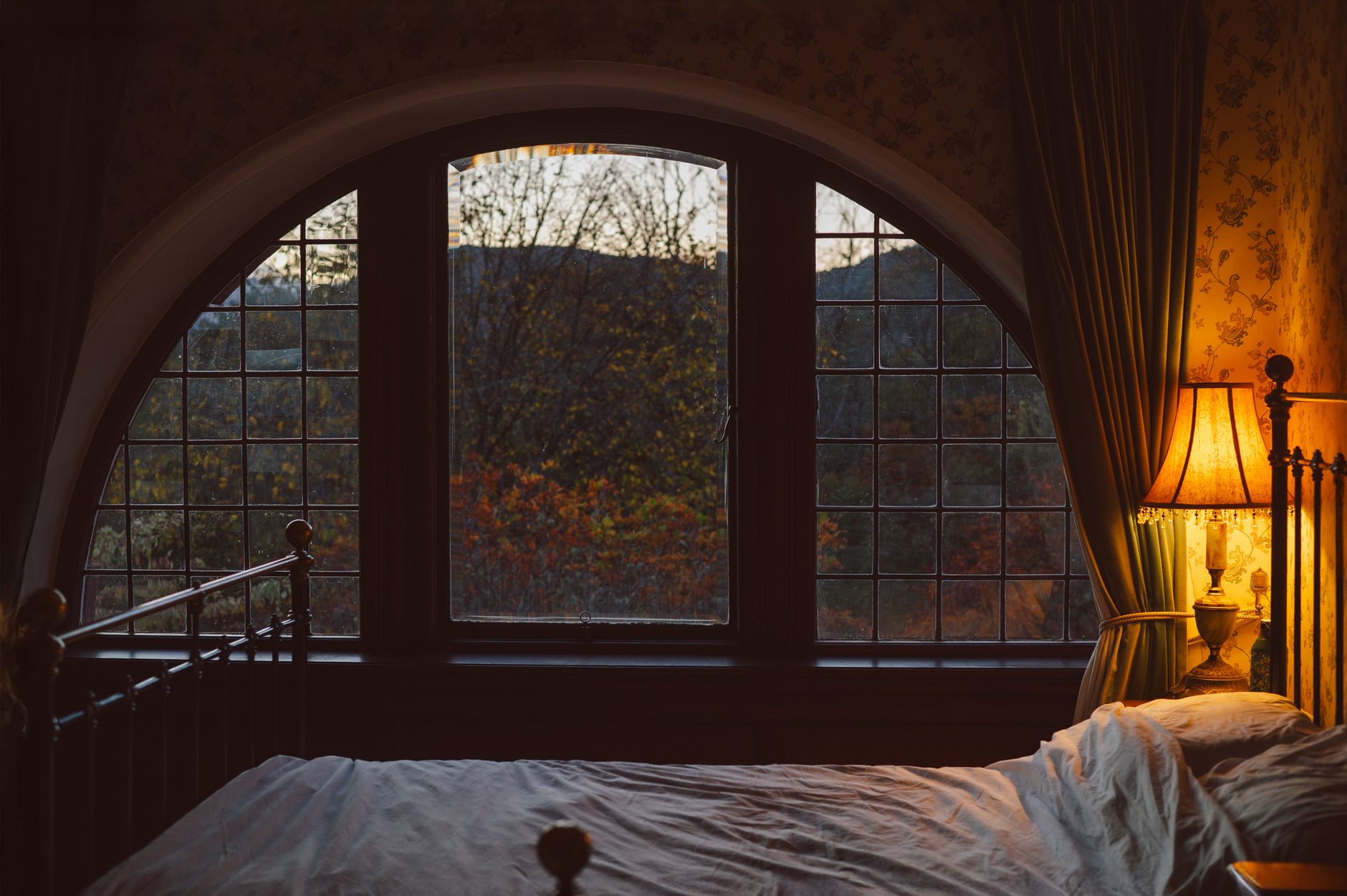 Fenêtre en arc d'une chambre avec vue sur des arbres d'automne, lampe allumée