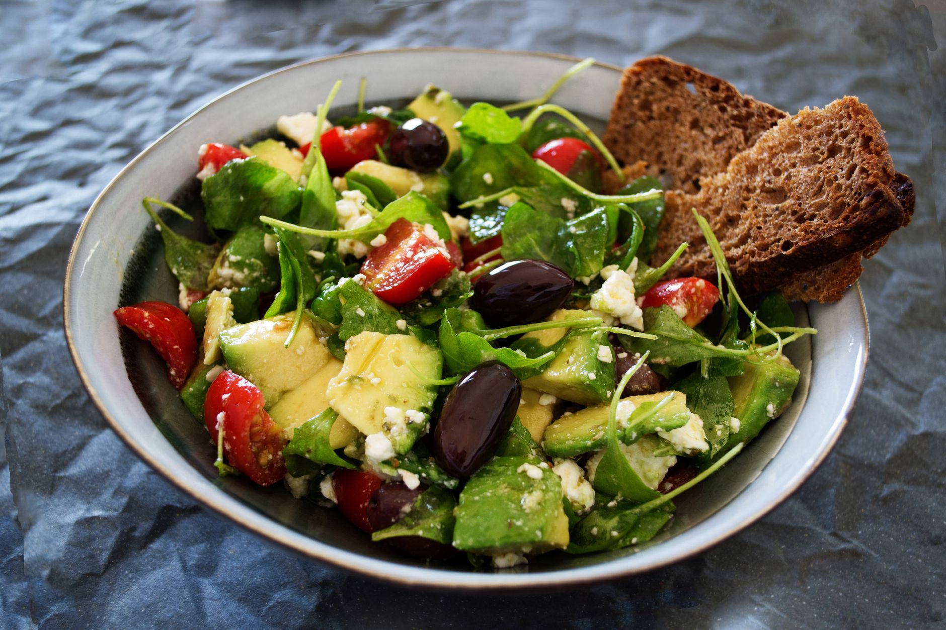 Salade d'avocat, tomates cerises et olives avec une tranche de pain complet