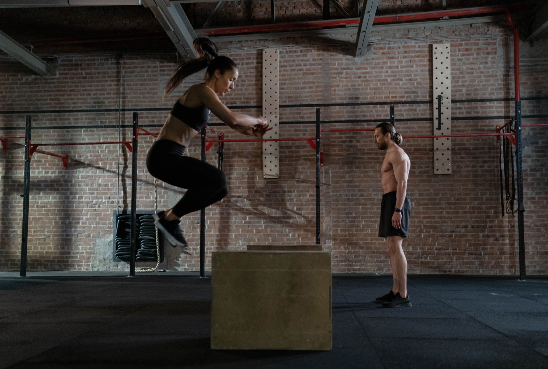 Athlète féminine effectuant un saut sur caisse en salle, coach observant.