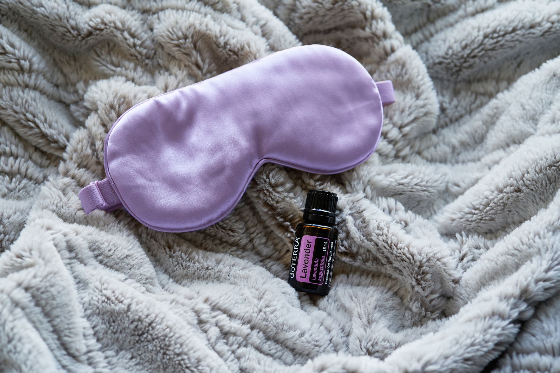 Huile essentielle de lavande et masque de sommeil violet sur couverture grise.