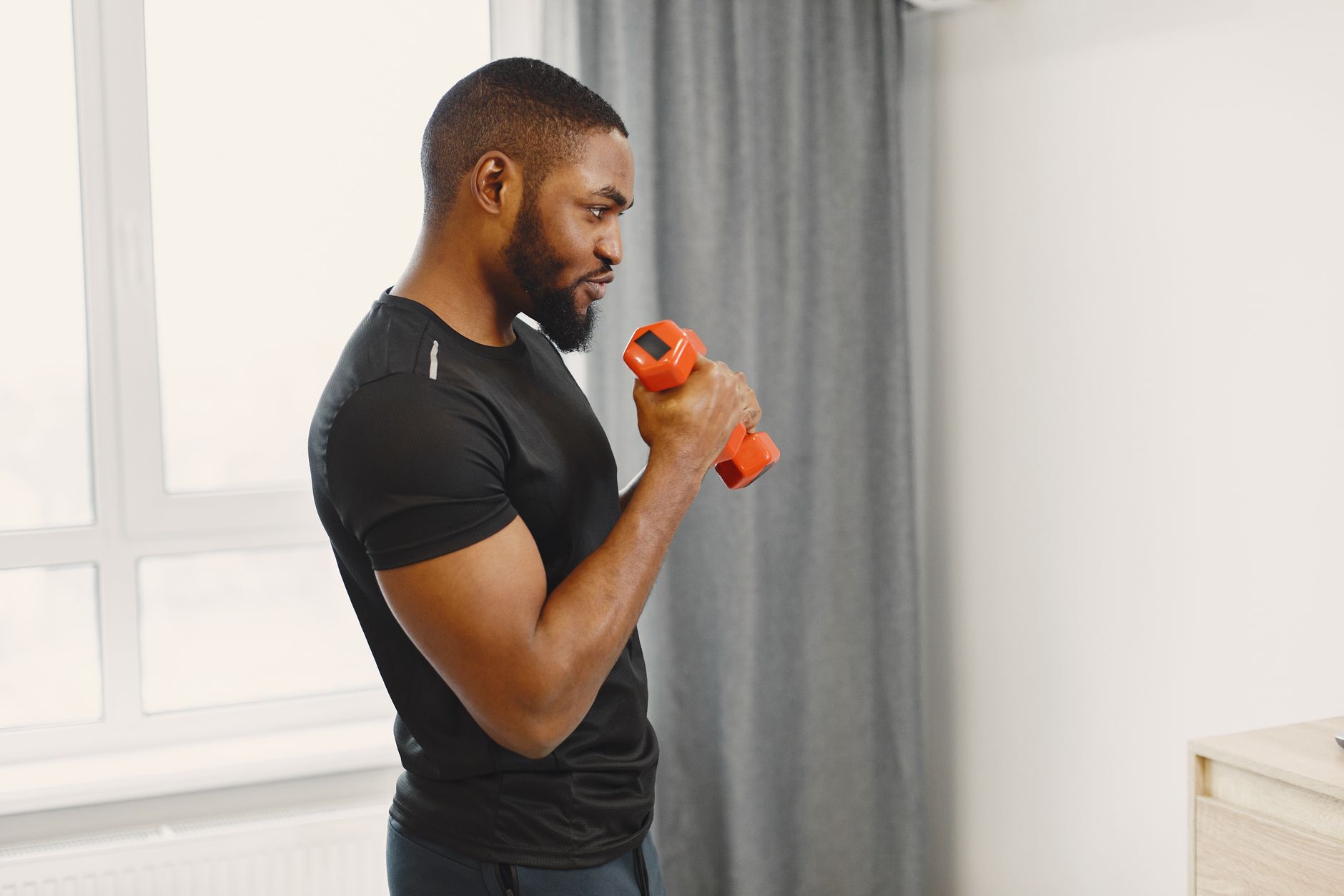 Homme afro-américain faisant de l’exercice avec haltère en intérieur.