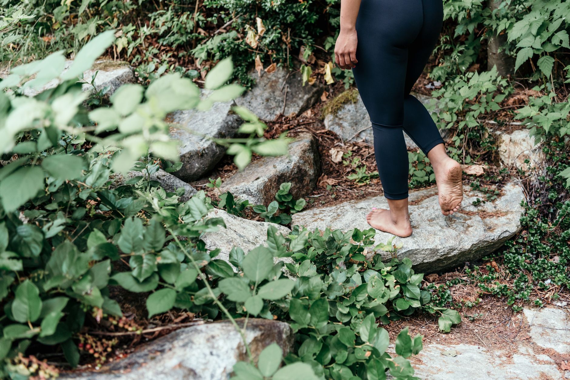 Adulte marchant pieds nus sur chemin rocheux entouré de verdure.