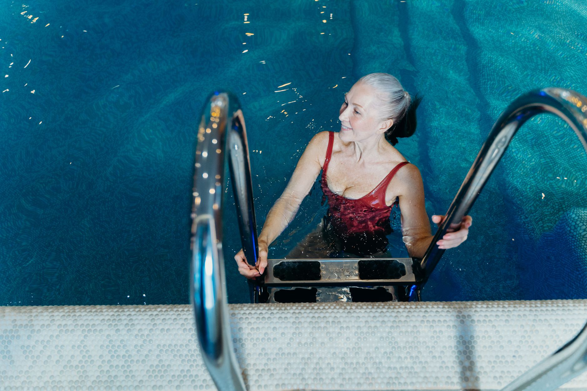 Femme âgée en maillot rouge souriant en sortant de la piscine.
