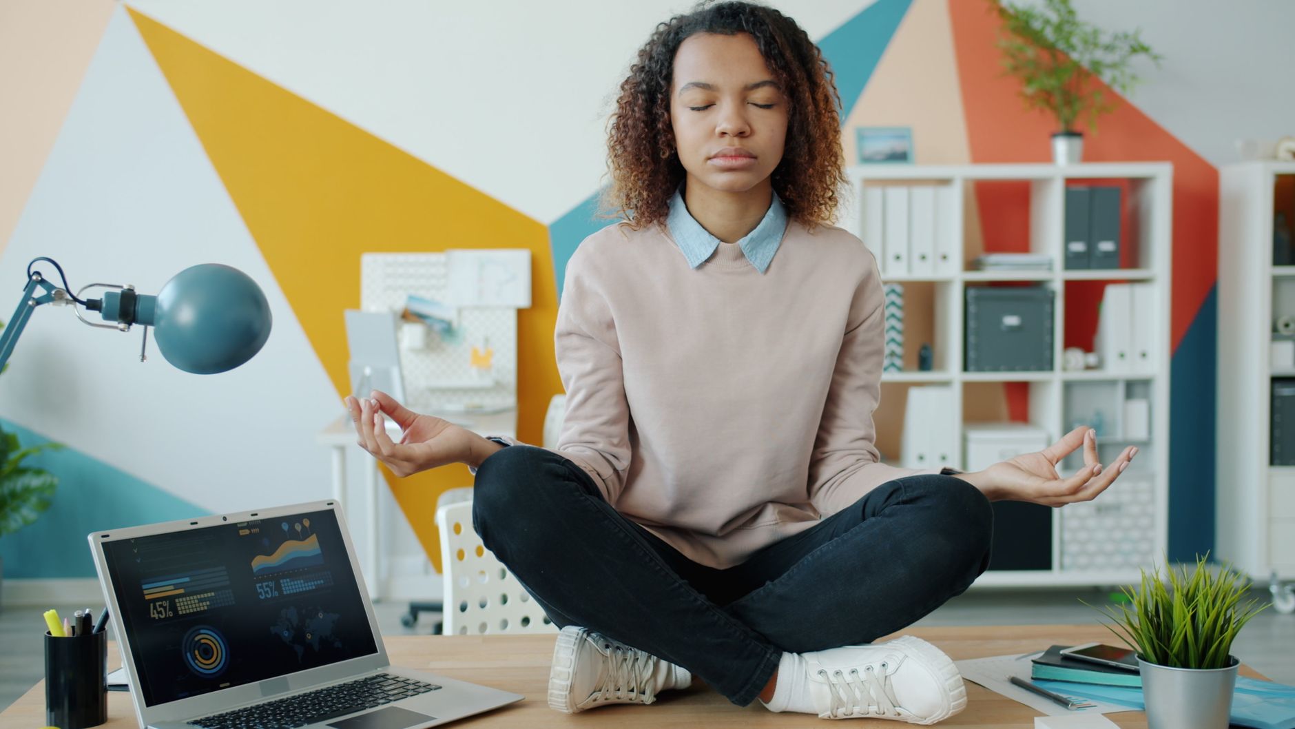 Jeune femme méditant jambes croisées sur bureau dans bureau moderne.