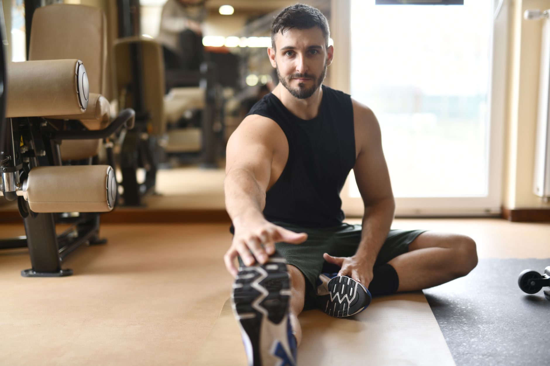 Homme en tenue de sport s’étirant au sol dans salle moderne.