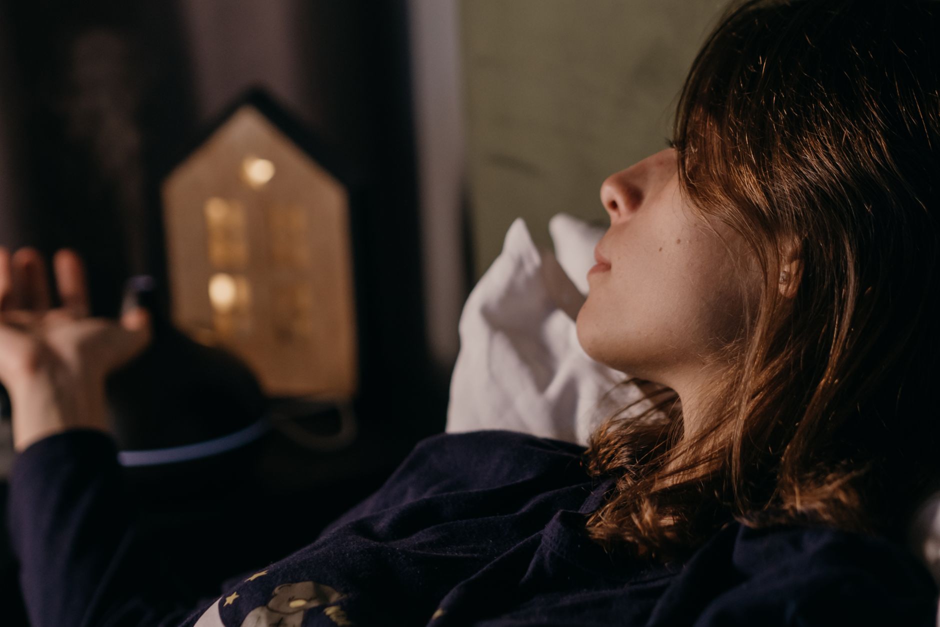 Femme sereine allongée dans un lit sous lumière douce la nuit.