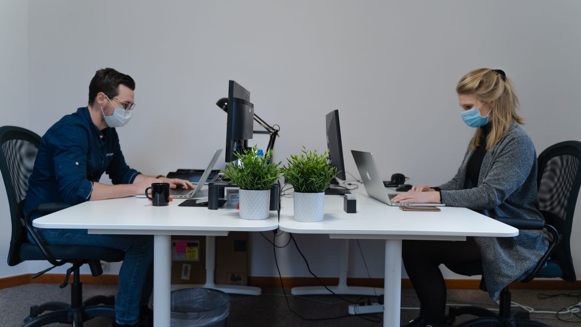 Deux employés portant masques travaillant sur ordinateurs en bureau séparés.