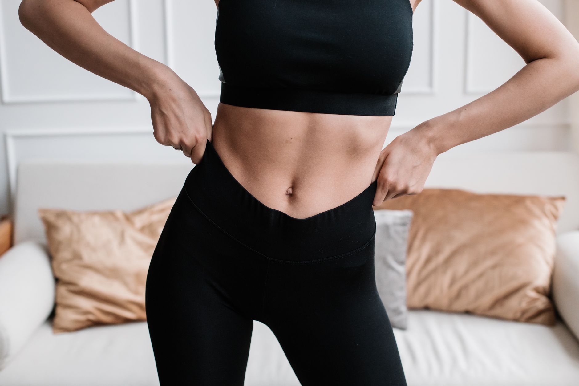 Gros plan d’une femme en tenue sportive ajustant son pantalon dans salon.