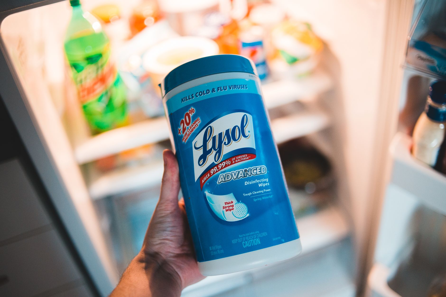 Personne tenant lingettes antibactériennes près d’un frigo ouvert.