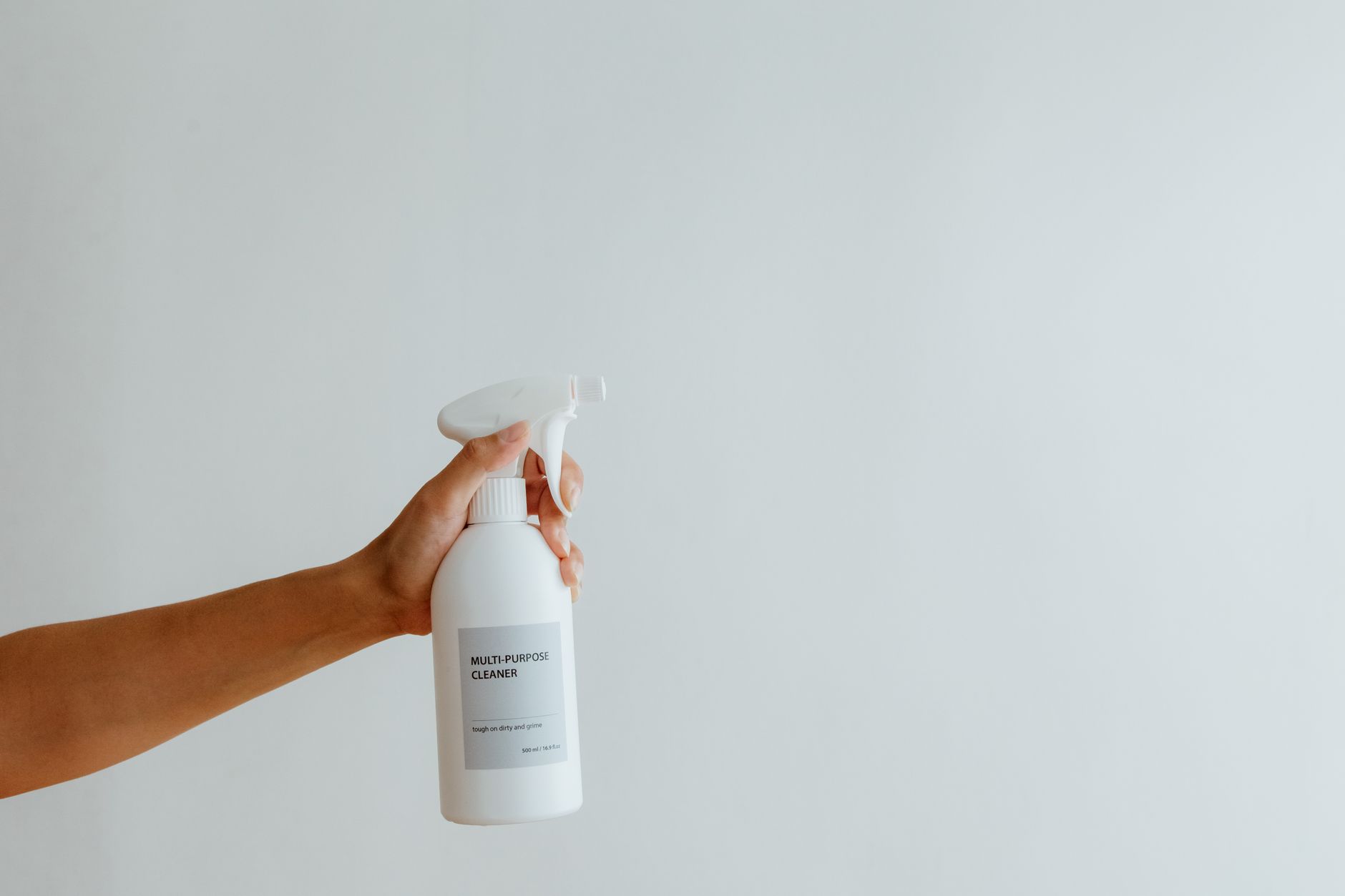 Gros plan d’une main tenant un spray nettoyant multi-usage sur fond blanc.