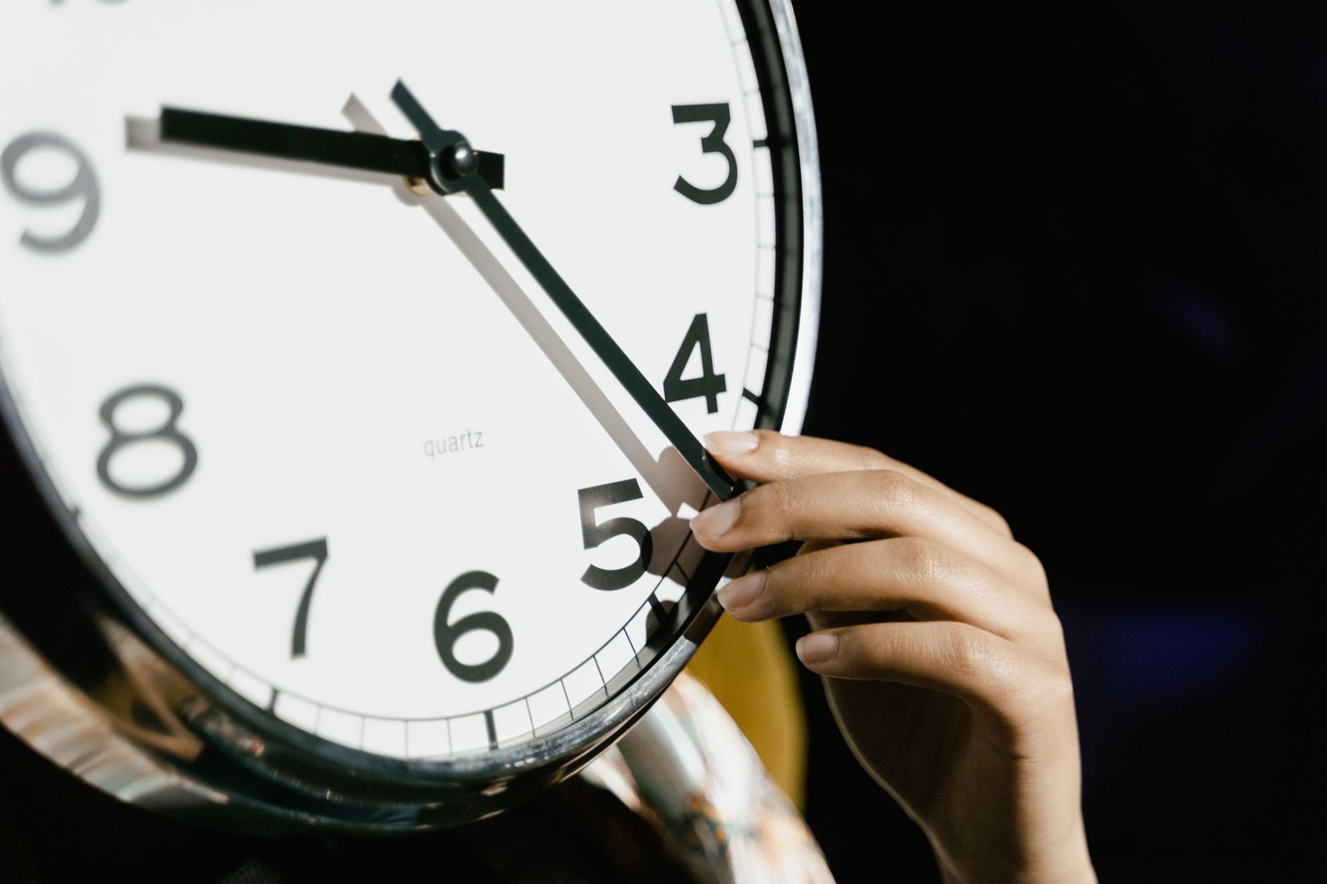 Main réglant l'heure sur une grande horloge analogique.