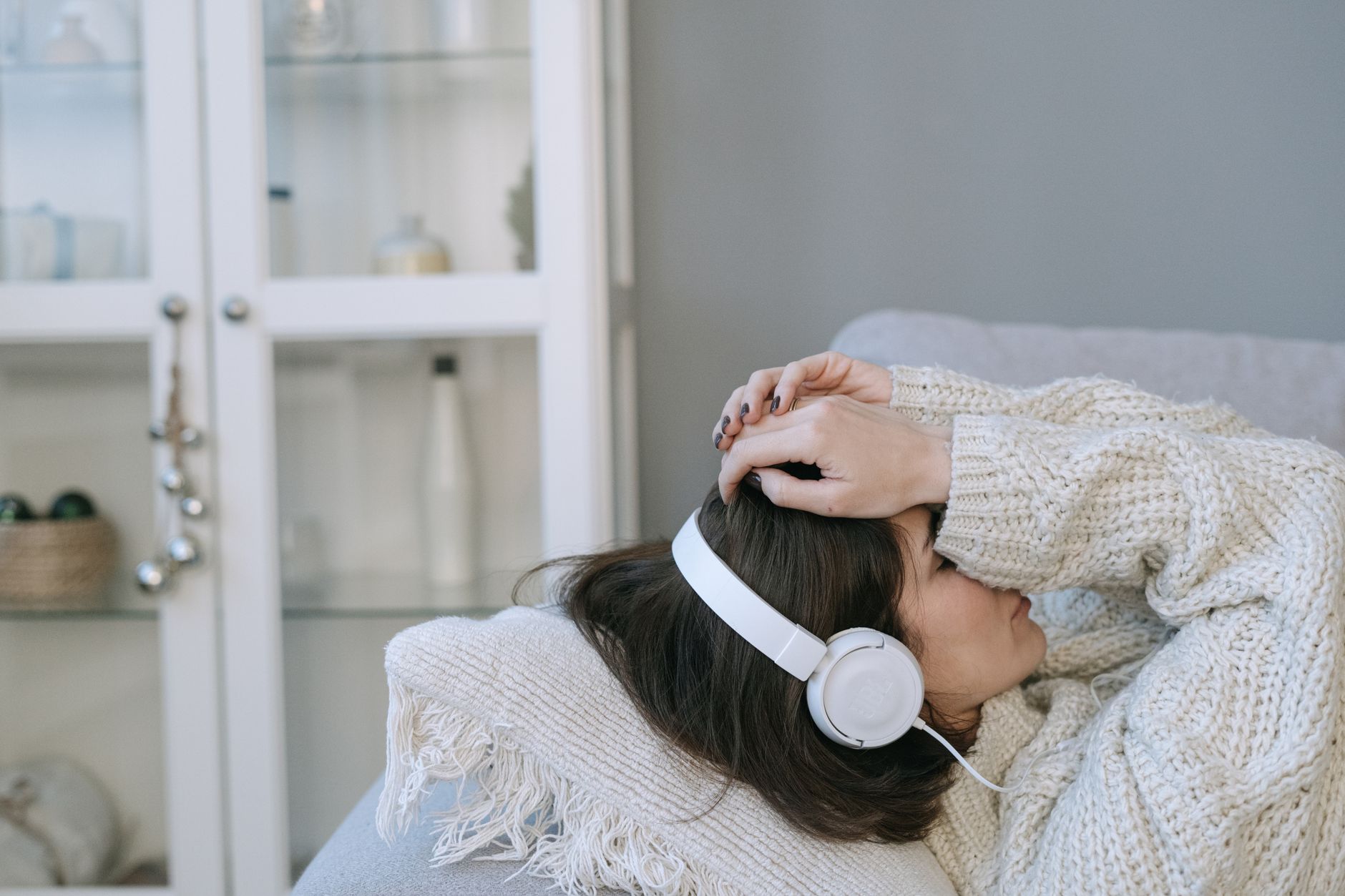 Femme en pull confortable portant casque audio allongée à l’intérieur.