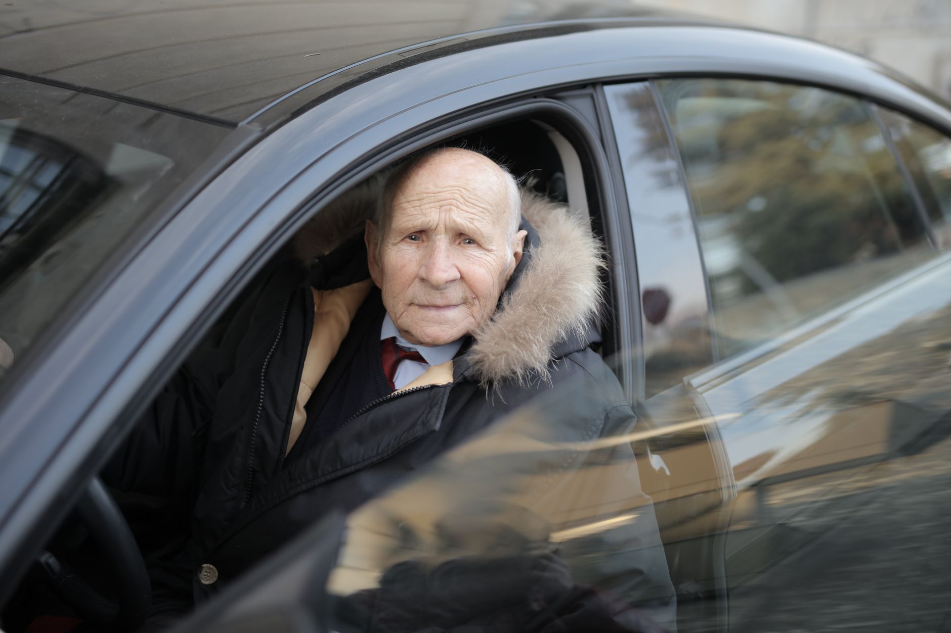 Homme âgé conduisant une voiture, manteau d’hiver, vu par la fenêtre.