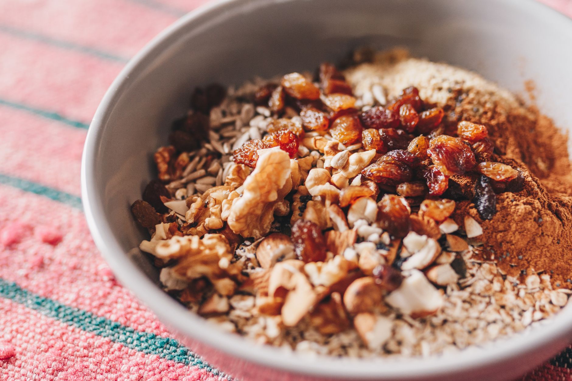bol blanc rempli de flocons d'avoine, de noix, de raisins secs et de cannelle posé sur une nappe rayée