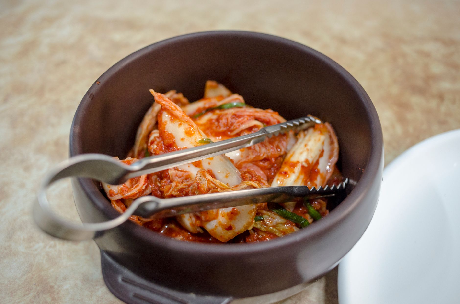 bol en céramique brune rempli de kimchi de chou chinois au piment, avec une pince de service en métal
