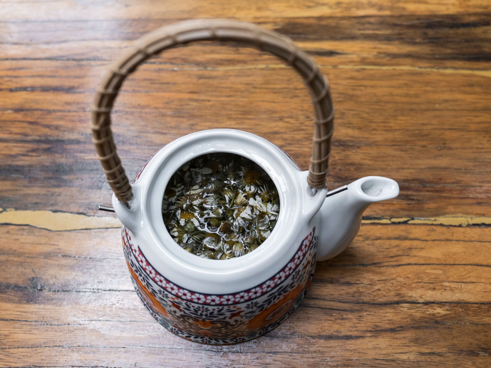 fleurs de camomille séchées qui infusent dans une théière en céramique posée sur une table en bois