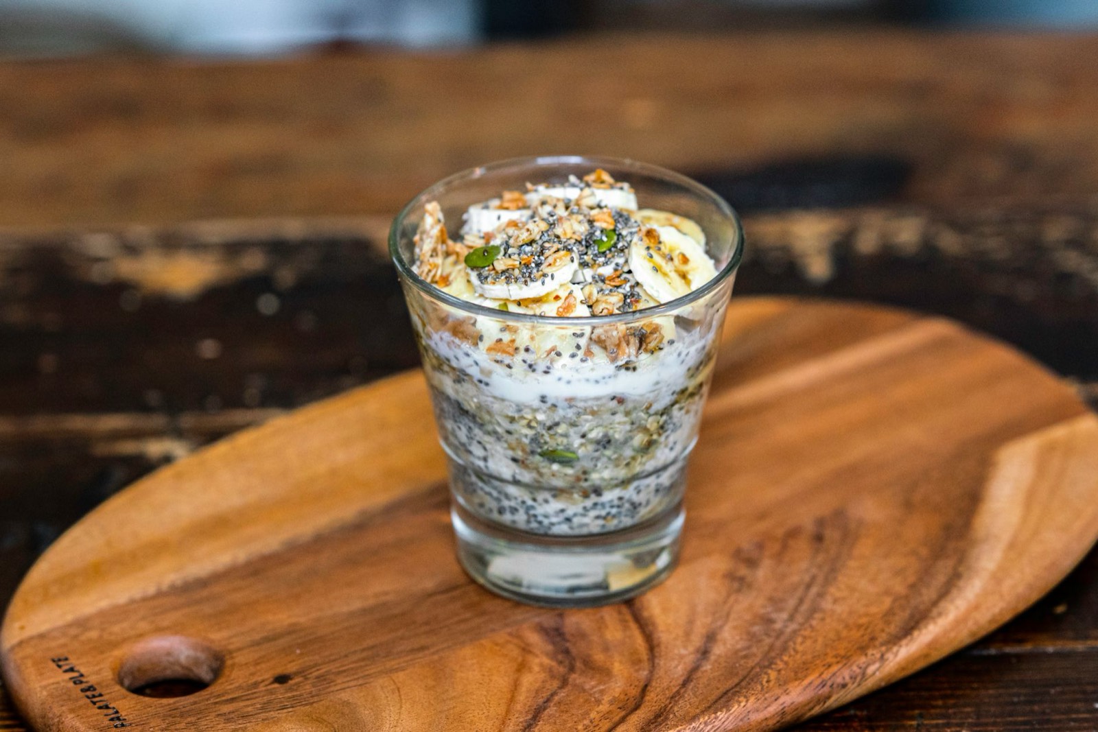 Bol de yaourt nature avec granola et graines, posé sur une table en bois